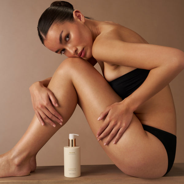 Model posing beside Tropic Summer Skin gradual tanning serum bottle.