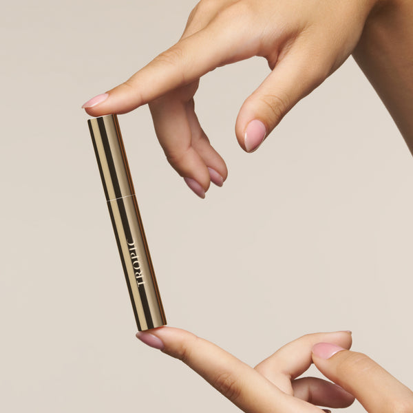 Hand holding the gold Lashful Eyelash Growth Serum against a soft neutral background, showcasing its sleek, premium packaging.