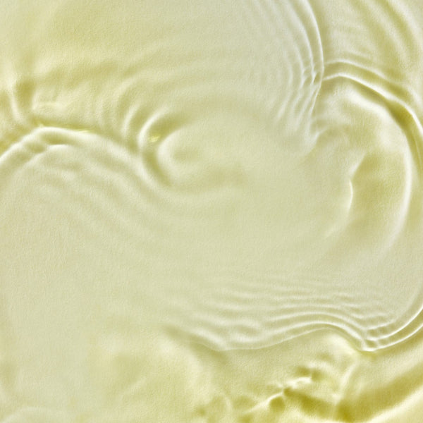 Close-up of Tropic Signature Oil’s silky golden texture with soft ripples and light reflections.