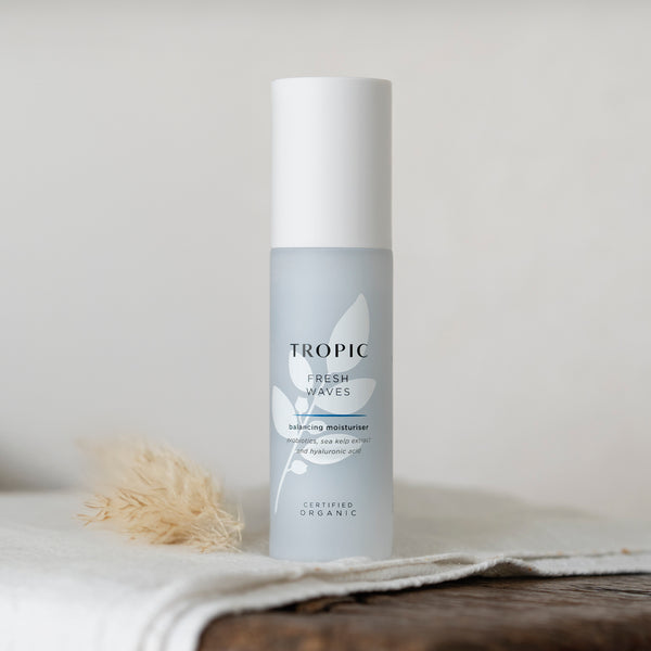 Tropic Fresh Waves Balancing Moisturiser bottle placed on a soft fabric surface with dried grass beside it, showcasing its clean, minimalist design that reflects its gentle, organic skincare formula.