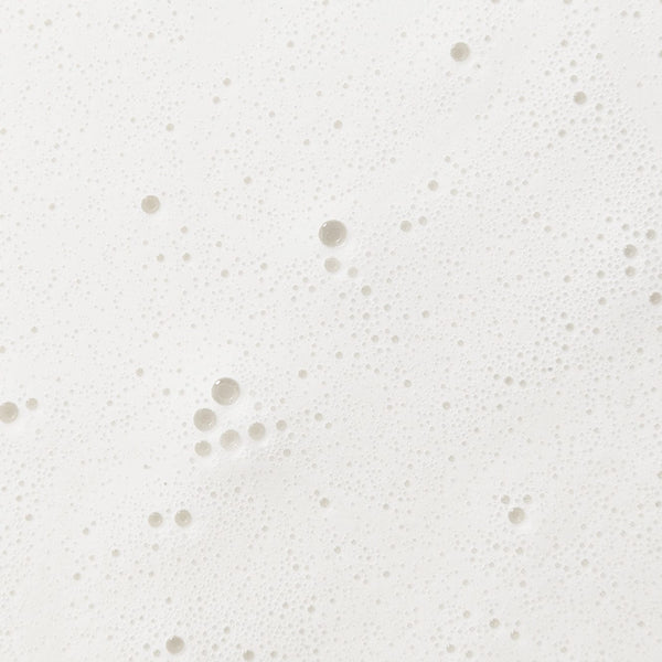 Close-up of a creamy white foamy texture with fine bubbles, representing the gentle formula of baby washing milk.