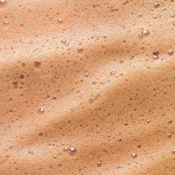 Close-up texture of Tropic Sun Drench tanning mousse, showing a smooth, foamy surface with fine bubbles and a warm bronze hue.