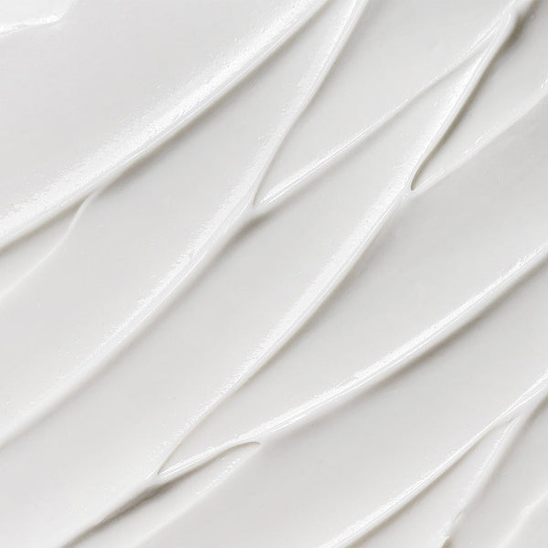 Close-up texture of smooth white cream with soft diagonal ridges and a glossy finish.
