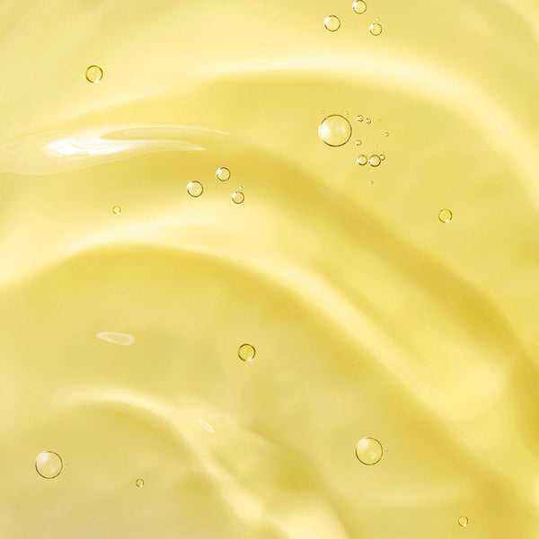Close-up of smooth golden-yellow baby oil texture with small air bubbles suspended in the liquid.