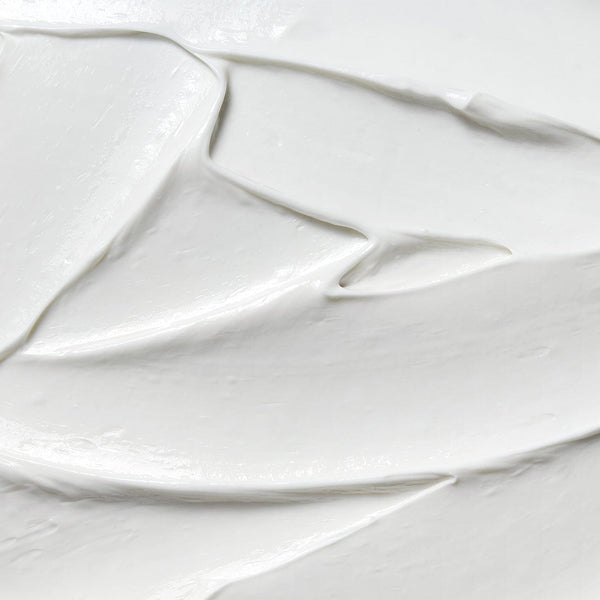 Close-up texture of smooth white cream with soft peaks and a glossy finish, showing the rich, nourishing consistency of a foot care formula.