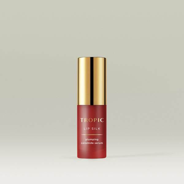 A sleek red bottle of Tropic Lip Silk plumping ceramide serum with a shiny gold cap, standing upright against a soft neutral background.