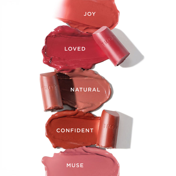 Five Tropic Butter Tint swatches labelled Joy, Loved, Natural, Confident, and Muse, with matching lipstick bullets displayed.