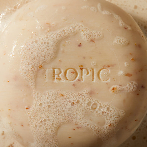 Close-up of a Cleansing Body Pebble with 'Tropic' embossed on it, surrounded by bubbles.