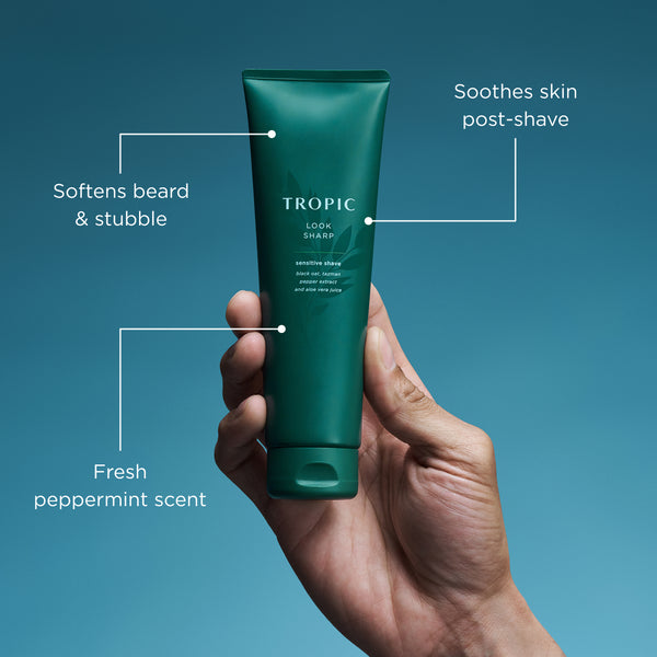Hand holding a green tube of Tropic skincare product with text on benefits against a blue background