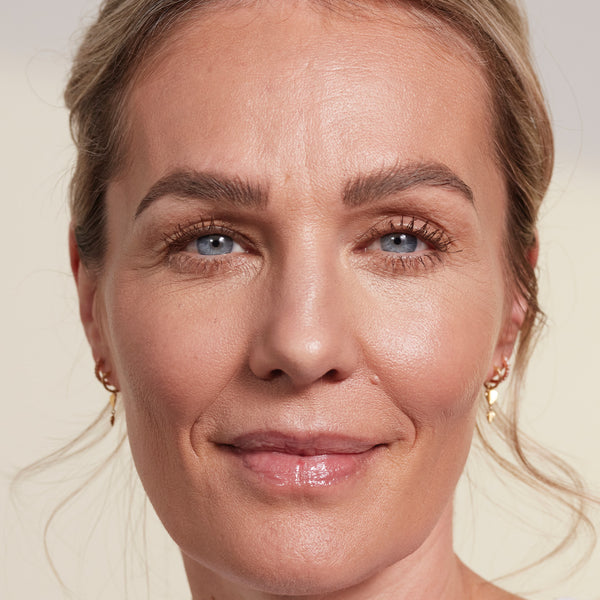 Close-up of a woman’s face showing a smooth, glowy makeup finish, with defined brows, subtle eye makeup, and glossy lips.