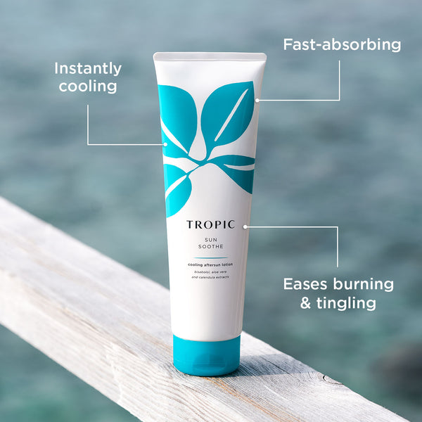 Tropic Sun Soothe cooling aftersun lotion tube on a wooden ledge by the sea, with text highlighting its instantly cooling, fast-absorbing formula that eases burning and tingling.