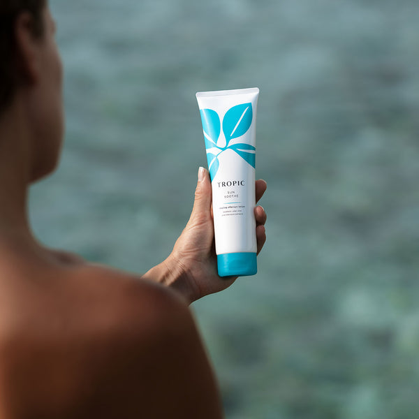 Person holding a tube of Tropic Sun Soothe cooling aftersun lotion near the ocean, highlighting the product’s soothing, refreshing qualities after sun exposure.