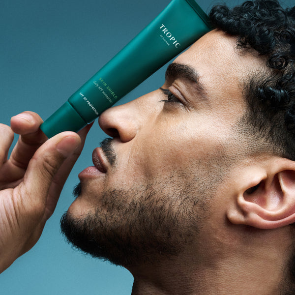 Model holding Tropic Skin Shield SPF moisturiser tube beside face.