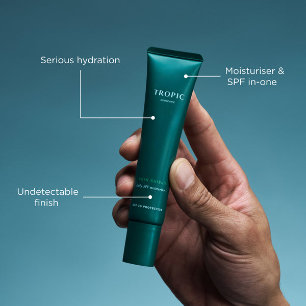 Hand holding Tropic Skin Shield SPF moisturiser tube with hydration and SPF benefit callouts.