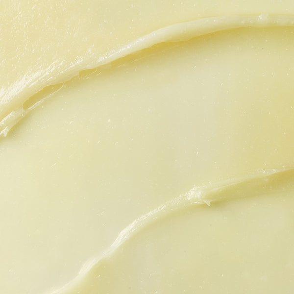 The image is a close-up of a smooth, creamy, pale yellow substance, likely a balm or butter. It shows a glossy texture with gentle curves, suggesting it has been spread or swirled. 