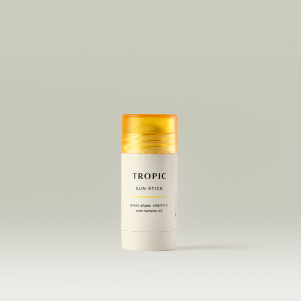 Tropic Sun Stick with green algae, vitamin E, and tamanu oil, shown in a sleek white tube with a yellow cap against a soft neutral background.