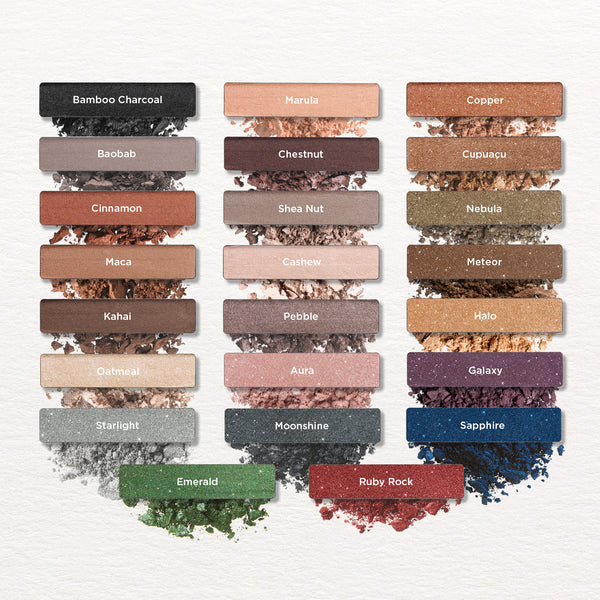 A collection of  Tropic “Eyes On You” eyeshadow swatches arranged in three vertical columns, each shade shown as a rectangular pan with its name and a crushed pigment texture beneath. Shades include Bamboo Charcoal, Baobab, Cinnamon, Maca, Kahai, Oatmeal, Starlight, Emerald, Marula, Chestnut, Shea Nut, Cashew, Pebble, Aura, Moonshine, Ruby Rock, Copper, Cupuaçu, Nebula, Meteor, Halo, Galaxy, and Sapphire.