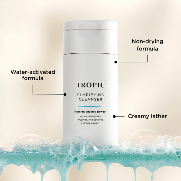 Tropic Clarifying Cleanser Foaming Enzyme Powder surrounded by light blue foam, with annotations highlighting its water-activated, non-drying formula that creates a creamy lather for gentle cleansing..