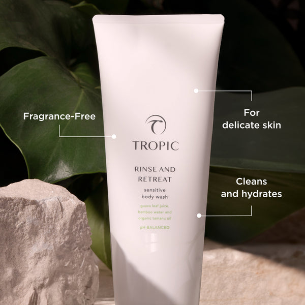 Tropic Rinse and Retreat Sensitive Body Wash tube displayed among natural stones and green leaves, highlighting its fragrance-free, pH-balanced formula for delicate skin that cleans and hydrates.