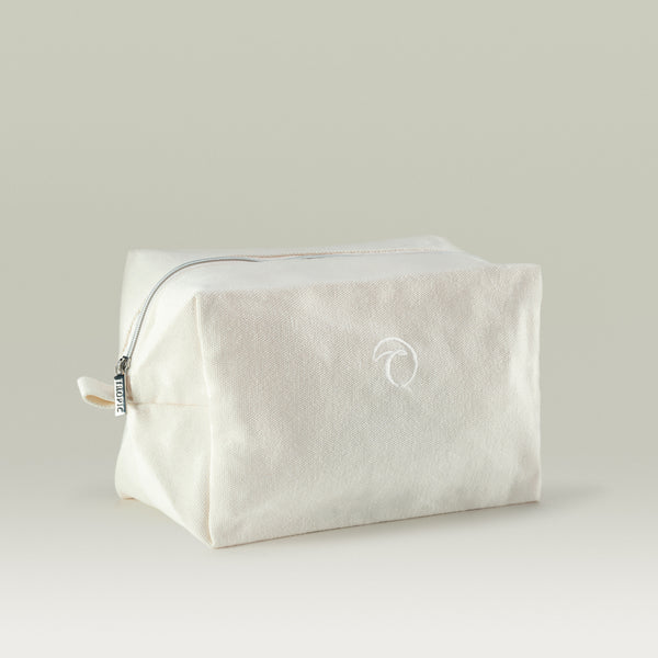 A minimalist beige Tropic toiletry bag made from fabric, featuring a subtle embroidered Tropic logo, silver zipper, and simple rectangular shape, displayed against a neutral background.