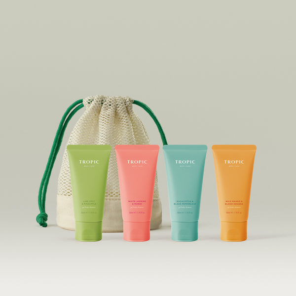 Four travel-sized Tropic Gel Body Cleansers in Lime Zest & Pineapple, White Jasmine & Monoi, Eucalyptus & Black Pepperleaf, and Wild Mango & Blood Orange, displayed alongside a reusable mesh wash bag.
