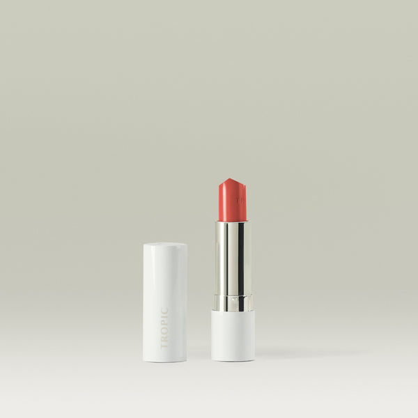 Tropic Butter Tint in a coral shade shown open beside its white casing on a minimal background.