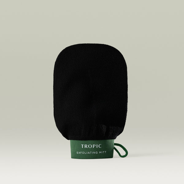 Tropic Exfoliating Mitt in black with a textured surface and green cuff, displayed upright against a neutral background with the Tropic logo visible on the label.