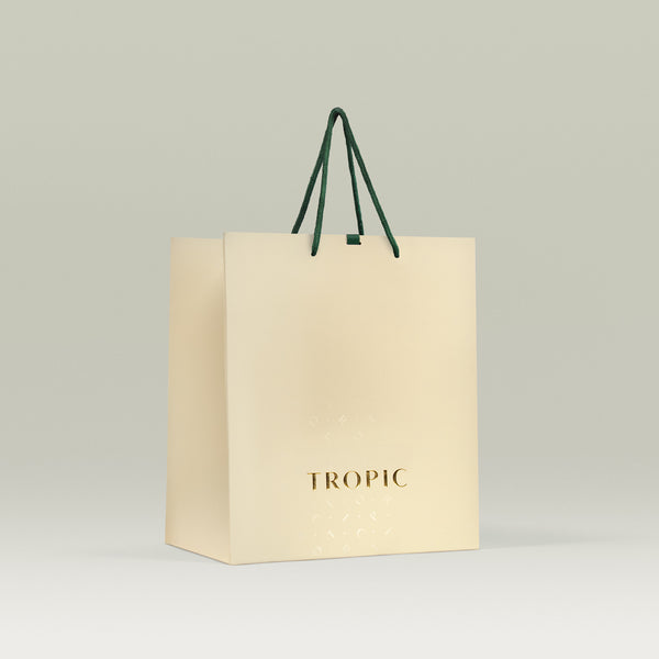Cream-colored Tropic gift bag with gold logo and dark green rope handles, displayed against a light neutral background.