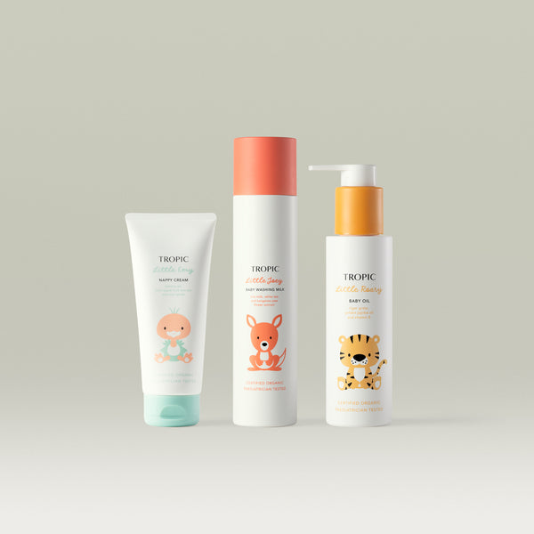 Packshot of three Tropic Little Heroes baby care products arranged side by side against a soft neutral background: Little Emy Nappy Cream, Little Joey Baby Washing Milk, and Little Roary Baby Oil. Each white bottle or tube features colourful illustrated animal characters, highlighting the gentle baby skincare collection.
