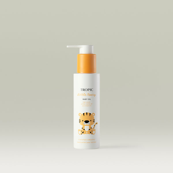 Tropic Little Roary Baby Oil bottle with orange pump and cute tiger illustration on a light background. Text reads “Tiger grass, golden jojoba oil and vitamin E.”