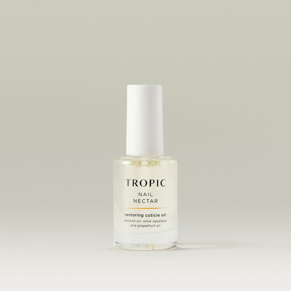 Transparent glass bottle of Tropic Nail Nectar restoring cuticle oil with a white cap, containing almond oil, olive squalane, and grapefruit oil, displayed on a neutral background.