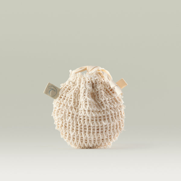Natural cotton mesh pebble pouch with a drawstring closure and Tropic tag, designed for storing and using cleansing pebbles.