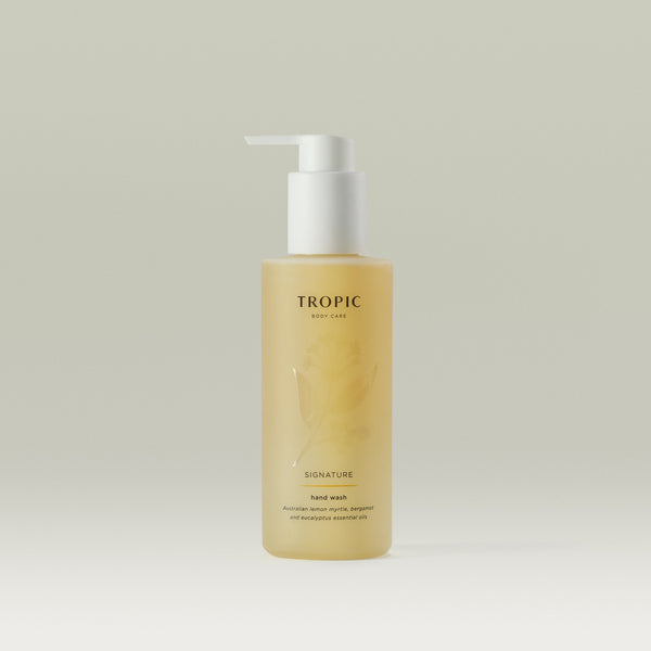 Tropic Signature Hand Wash bottle with a pump dispenser, filled with golden-yellow liquid. The label highlights Australian lemon myrtle, bergamot, and eucalyptus essential oils.