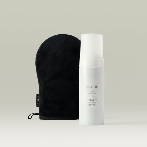 Tropic Sun Drench Overnight Tanning Mousse bottle displayed beside a soft black Tropic tanning mitt, shown on a neutral background.