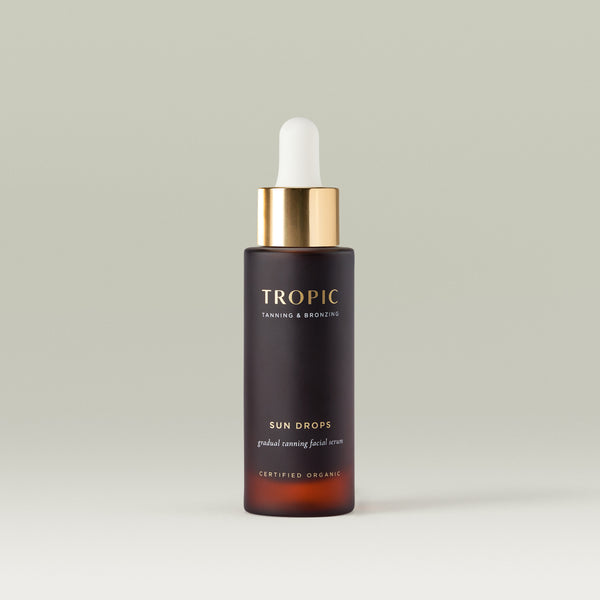 Packshot of Tropic Sun Drops Gradual Tanning Facial Serum in a dark amber glass bottle with a gold dropper cap, centred against a soft neutral background. The product is shown alone, highlighting its minimalist design.
