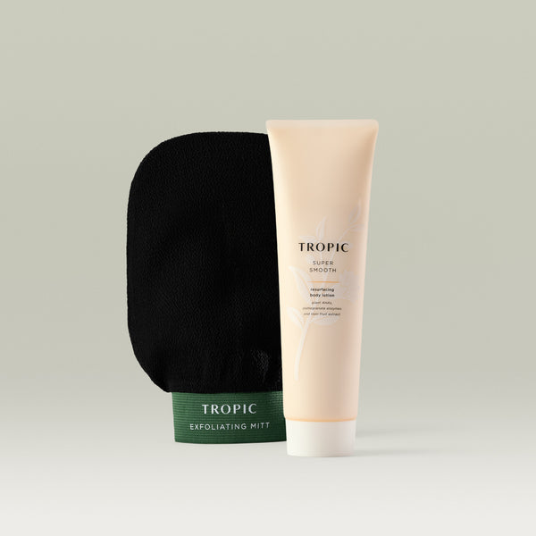 A tube of Tropic Super Smooth Resurfacing Body Lotion and a Tropic Exfoliating Mitt. The body lotion comes in a peach-colored tube and is formulated with plant AHAs, pomegranate enzymes, and noni fruit extract, highlighting its exfoliating and smoothing properties. The exfoliating mitt is black with green trim.