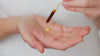 Model has a small amount of Skin Feast Moisturiser in the palm of their hand. They add a few drops of sun drops from the pipette on top. They rub together and begin to apply to their face.