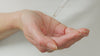 Model uses a pipette to drop a few drops of fruit peel into the palm of their hand. They then press into their face.