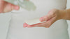 Model shakes Juicy greens bottle to disperse product onto a damp forest leaves pad. They then apply the product on the pad to their face sweeping across cheeks, forehead and chin.